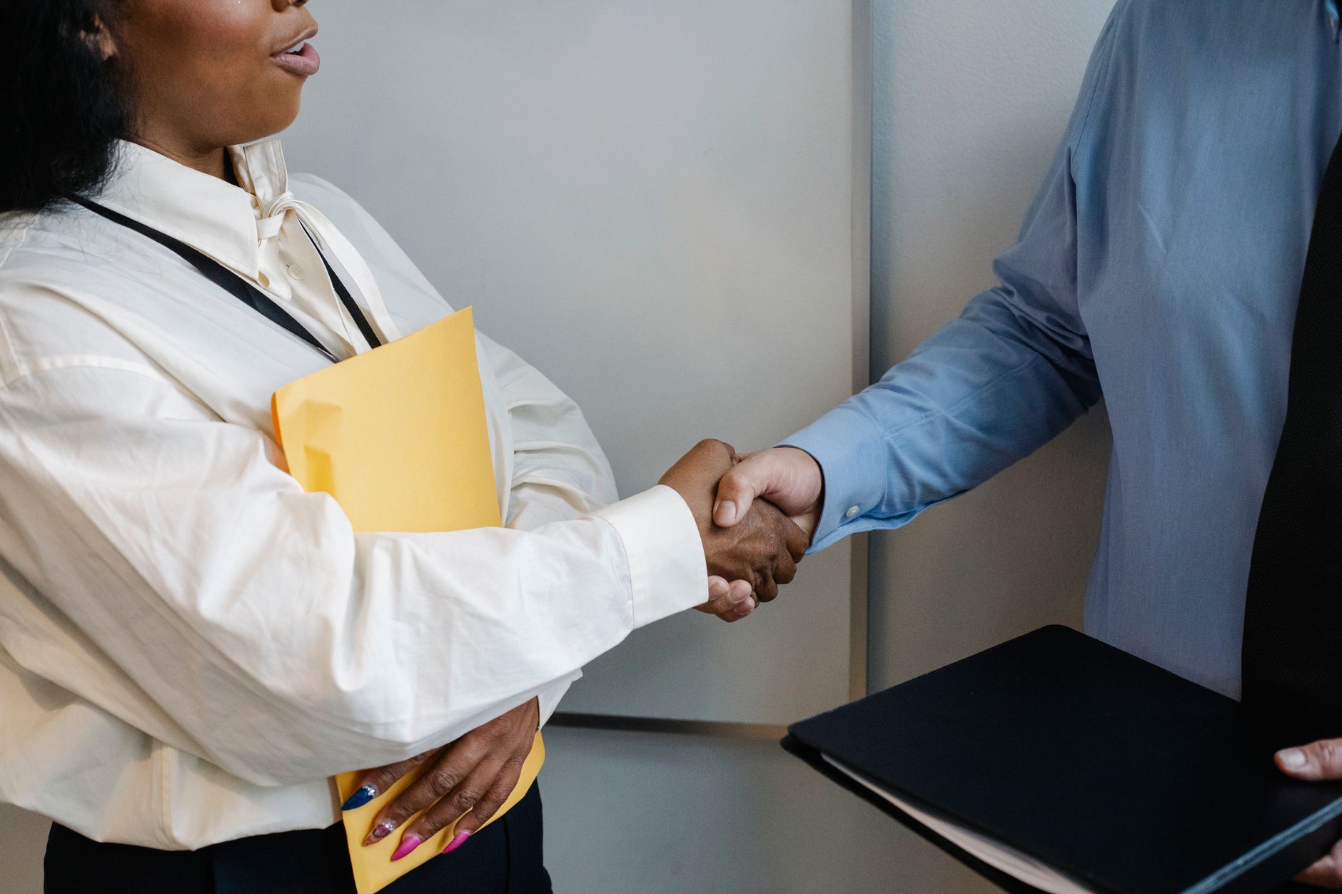 Poignée de main entre deux personnes en tenue de bureau, l’une avec une pochette jaune, l’autre avec un dossier noir.